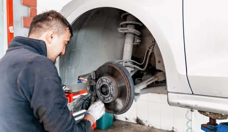 A mechanic checking for mechanical failures after a car accident. He has removed the tire and is checking the car parts.