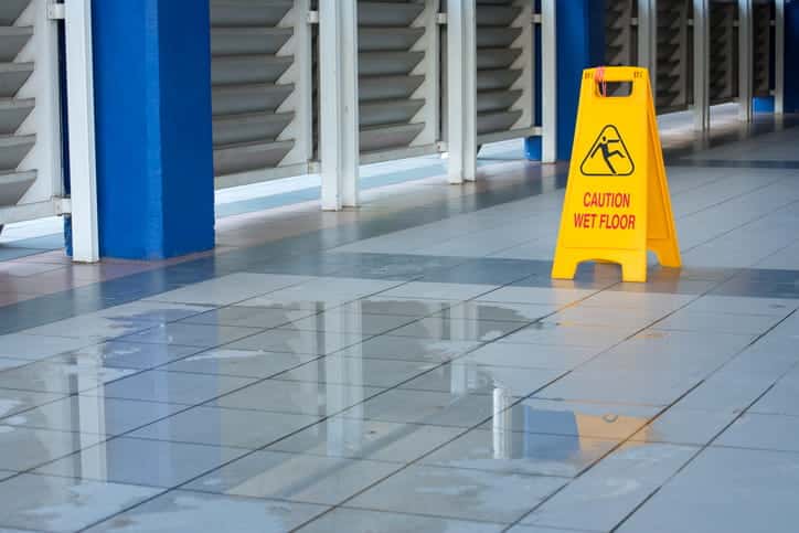 A Caution Wet Floor Sign Next To A Puddle Inside A Business. 